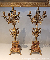 Pair of gilt metal candelabras with pink marble bases and detailed decoration, shown side by side.