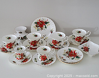 Front view of Royal Albert Poinsettia fine china tea set including cups, saucers, plates and a vase arranged on a table against a plain background.
