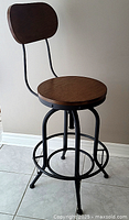 Front angled view of the stool showing wooden seat and backrest, black metal frame, and footrest ring.