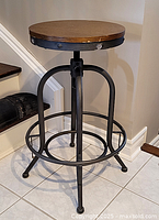 Full view of the stool showing metal frame with circular footrest and wooden seat.