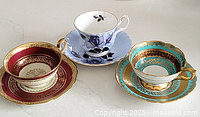 Three decorative teacups with matching saucers displayed on a white surface.
