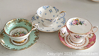 Group photo showing three different teacups and matching saucers with floral patterns and gold detailing