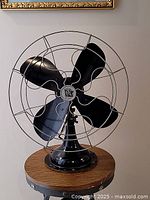 Front view of large vintage electric fan showing black blades, grey cage, and black base on wooden surface