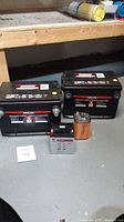 Photo of 4 batteries: 2 large Kirkland automotive batteries, 1 smaller rectangular Mallory industrial battery with terminals, 1 9V battery in the group.