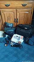 Canon digital camera, Canon 8mm video camcorder, JVC camcorder, camera bags, power cords, AV cables, and manuals displayed on blue carpet