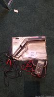 Digital timing light packaged with attached leads and a handheld multimeter with cables on carpeted floor.