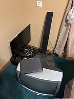 Corner view showing multiple electronics including a Samsung flat screen TV, a Citizen CRT TV, and a tall Insignia speaker.