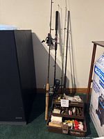 Front view of four rods standing beside tackle box loaded with fishing lures and bobbers