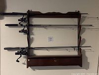 Horizontal wooden fishing rod rack holding three fishing rods with reels, showing the locked drawer without key