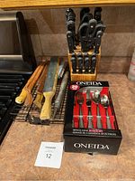 Full view of kitchen utensils including wooden handled knives, metal blades, knife block with knives and scissors, Oneida 20-piece cutlery boxed set on kitchen counter