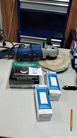 Full lot with polisher/sander on table with polishing bonnet attached and packaging boxes in front showing bonnets included.