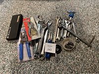 Wide view of the tool assortment including dial caliper case, multiple wrenches, pliers, sockets, and a flexible square.