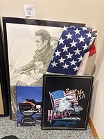 Photo showing four framed prints leaning against wall and partially folded American flag featuring motorcycle print beside them.