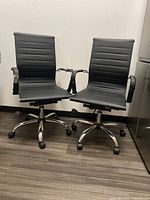 Two black modern office chairs side by side showing overall shape, seat, backrest, chrome bases, and frayed armrests.