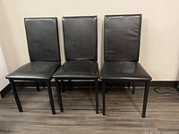 Front view of three of the four chairs showing dark espresso padded seats and backs with metal legs.