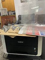 Photo of Brother all-in-one printer with clipboards and plastic sign holders stacked on top