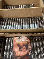 Three cardboard trays each containing approximately 20 shrink-wrapped copies of the DVD set, spines visible