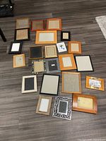 Top-down view of 21 assorted picture frames on floor, showing various sizes, colors, and materials.
