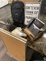 Photo shows 3 cork bulletin boards with aluminum frames stacked, Cisco phone on box, black coffee pod stand, Osprey backpack with UBS logo, metal sign reading 'DON'T EVEN THINK OF PARKING HERE', and other office items on a table.