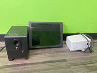 Front view of Logitech subwoofer, monitor and APC surge protector on wood surface against green wall