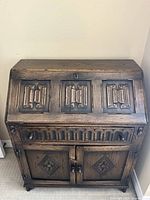 Front exterior view of antique wooden secretary desk showing carved panels and keyhole.