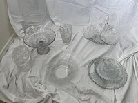 Overview of six assorted crystal and glass pieces including bowls, vases, and plates with different etched and textured patterns on white fabric background.