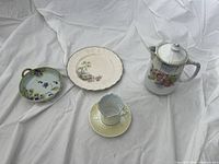 Full view of assorted porcelain china pieces including plate, teapot, cup and saucer, and small handled dish with floral designs