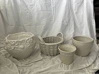 Four ceramic decorative pots arranged on fabric backdrop showing off-white color and traditional styles