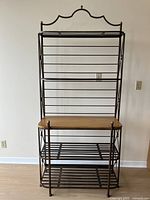 Front view of the baker's rack showing metal frame and wood flat middle shelf with metal slat shelves below.
