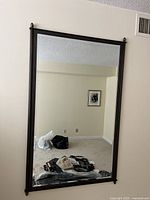 Full view of large rectangular mirror hanging on a beige wall above carpeted floor showing the entire frame and reflective surface in a bedroom setting.