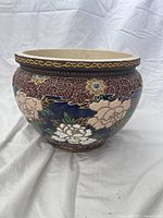 Side view of the medium ceramic pot showing blue background with beige and white floral patterns and decorated maroon rim with gold wavy design.