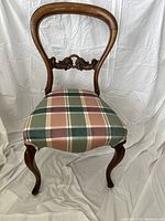 Front view of the vintage chair showing carved wooden backrest and multicolor plaid upholstery on the seat.