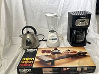 Full lot image showing Salton electric kettle, Osterizer blender, Cuisinart coffeemaker and boxed Salton hot tray in front.