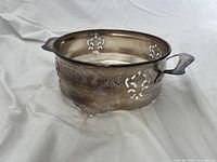 Side angled view showing engraved floral, scroll patterns, cutout design, handles, and feet