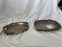 Two silver-plated trays placed side-by-side on a white background showing tarnish and wear