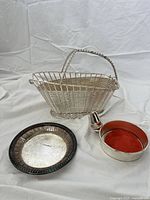 Full lot view showing three items: the wine bottle holder basket, coaster with stopper and felt lining, and the decorative silver coaster with patina.