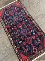 Full front view of rug laid on wooden floor showing overall geometric pattern, color and fringe