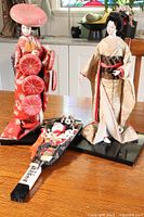 Front view of two standing Asian dolls and one mounted figure on a post showing detailed traditional garments and bases.