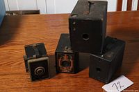 Four vintage box cameras on wooden surface showing front and top views