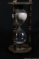 Side view of the decorative brass hourglass showing displaced white sand in upper bulb.