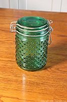 Front angled view of the collectible green hobnail textured glass mason jar with metal clamp lid on wooden table.