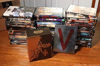 Overview of all DVDs in the lot stacked on a wooden surface including Star Wars boxed set and V series steelbook case