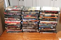 Photo showing the lot of 63 DVDs stacked in three columns on a wooden floor, titles visible on cases