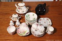 Overview of the full set showing varied pieces: teapots, cups, saucers, small plates, sugar bowl, salt and pepper shakers arranged on wooden table.