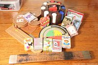 Photo showing wooden cribbage boards, poker chip holder with chips, multiple card games including Hearts, Animal Rummy, Old Maid, Avon, Anheuser, and other specialty decks along with a circular spinner game
