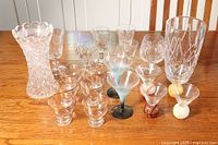 Photo of overall glassware lot showing large vase, shot glasses with sports ball stems, martini glasses, and clear stemware arranged on wooden table