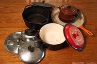 Overview of cast iron pots and pans, ceramic vessel, and pot lids on wooden surface.