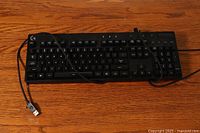 Full front view of Logitech G810 keyboard on wooden surface, showing all keys and USB cable with Logitech logo on connector.