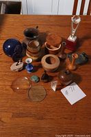 Photo shows a lot of miscellaneous collectibles arranged on a wooden table including wood vases, boxes, glass items, and a trophy.