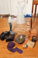 Wide angle showing all lot items on wood table: two display dolls, brass dish, purple scarf, coin purse, oriental box, glass bottle, and other small items.